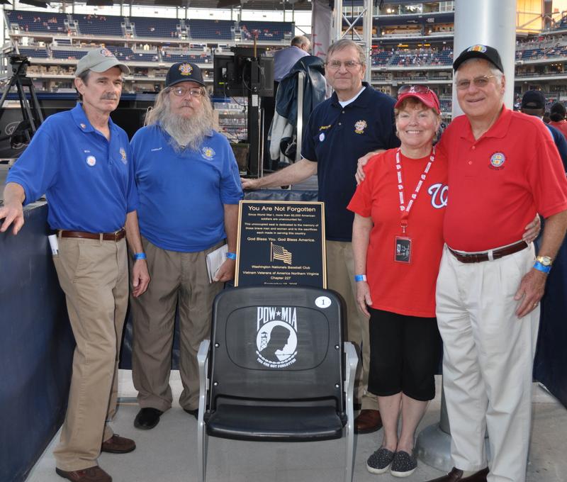 Five chapter members standing beside a POW/MIA chair and dedication plaque in the stands at Nationals Park.