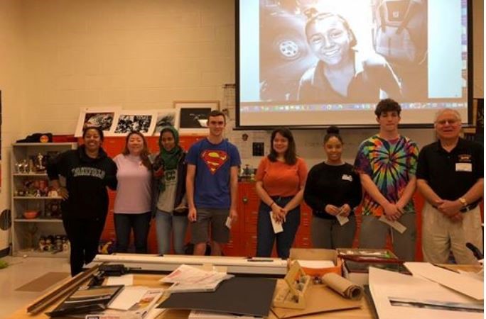 A chapter member stands with eight high-school students in an art classroom during a student awards presentation.